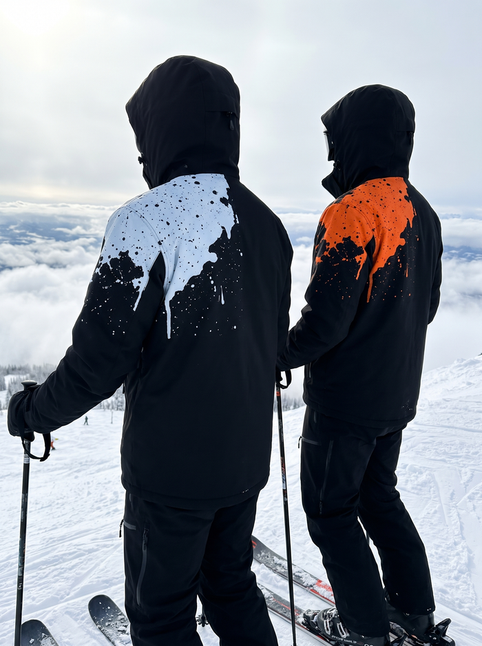 Two skiers at the top of a run in the Glacier White and Blaze Orange colorways