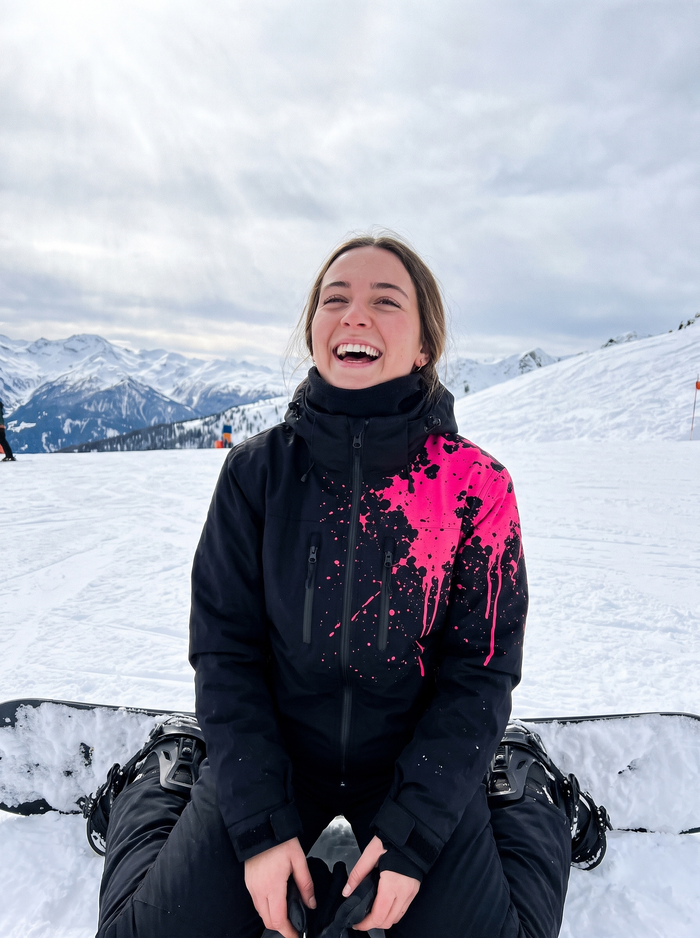 Snowboarder strapping in, wearing the StormShift jacket in Neon Pink